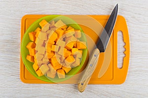 Cubes of raw pumpkin in bowl, knife on cutting board
