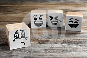 Cubes with sad and funny faces on wooden table. Bullying concept