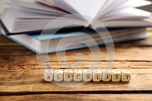 Cubes with word Blacklist and notebooks on wooden table, closeup