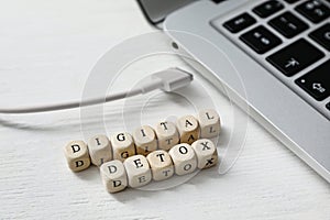 Cubes with words DIGITAL DETOX and disconnected charging cable on white wooden background