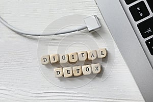 Cubes with words DIGITAL DETOX and disconnected charging cable on white wooden background, flat lay