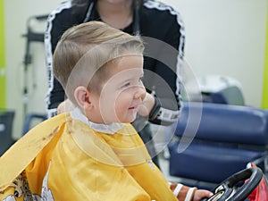 Cucasian brunet toddler on the haircut with a professional children's hairdresser. Little boy having a stylish