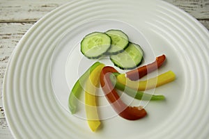 Cucumber and Bulgarian red green yellow pepper slices on white plate