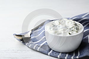 Cucumber sauce in ceramic bowl and spoon on wooden background, space for text