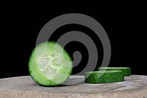 Cucumber slices on a wooden cutting board on black background