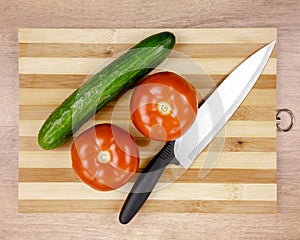 Cucumber and two tomatoes and a chef`s knife on the cutting Board. Ingredients for the salad. Healthy diet.