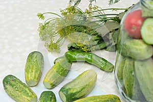 Cucumbers with green hot pepper on the table with glass jar with pickled vegetables cucumber and tomato with herbs and