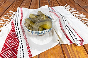 Cucumbers pickled in Romanian traditional clay bowl and traditional towel on wooden table