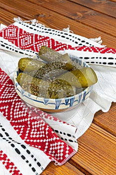 Cucumbers pickled in Romanian traditional clay bowl and traditional towel on wooden table