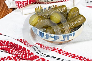 Cucumbers pickled in Romanian traditional clay bowl and traditional towel on wooden table