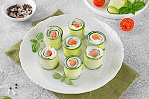 Cucumbers rolls with cream cheese, salted salmon and fresh herbs served on a white plate on a concrete background. Selective focus