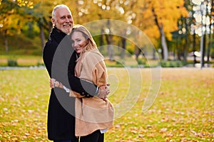 Cuddling old man and young woman outdoors in fall in daytime