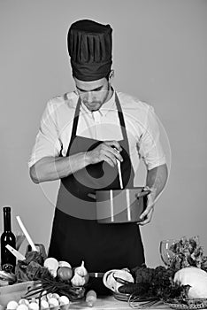 Cuisine and professional cooking concept. Chef with busy face holds red saucepan on grey background.