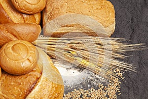 Culinary background with bread,sweet bun,wheat ears,grains on a black background, top view