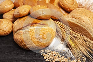 Culinary background with bread,sweet bun,wheat ears,grains on a black background, top view