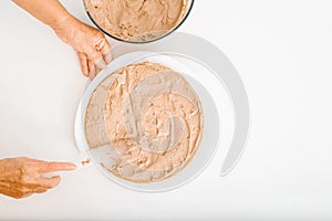 Culinary confectionery hobby. Top view female cook's wrinkled hands decorating cake with cream filling using spatula