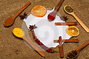 Culinary recipe concept. Piece of paper on sackcloth background. Cinnamon, dried orange and pepper, star anise around