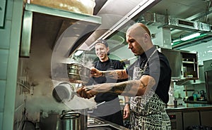 Culinary school. Handsome and confident chef teaching how to cook his two assistants in a restaurant kitchen