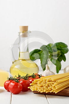 Culinary still life with dry pasta bucatini, fresh tomatoes and basil, bottle of oil on light background.