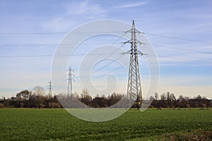 Cultivated field with electricity pylons and over head cables on a cloudy day in the italian countryside