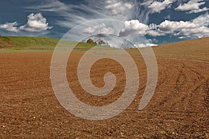 Cultivated plowed field at dusk under cloudy sky