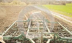 Cultivator behind tractor on ploughed soil near green field