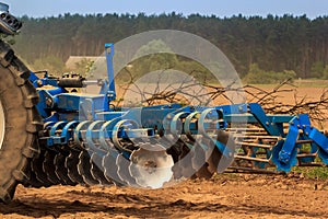 cultivator on ground road by ploughed field against village