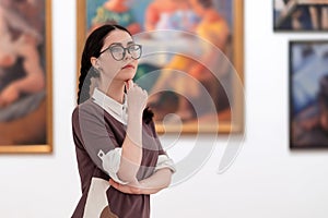 Cultural education and excursion. Portrait of caucasian pretty young woman wearing glasses contemplates arts. Defocused