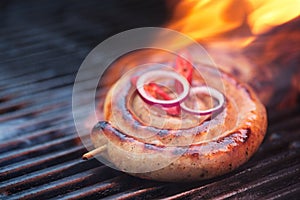 cumberland sausage, spiral pork sausage on bbq grill with flame,