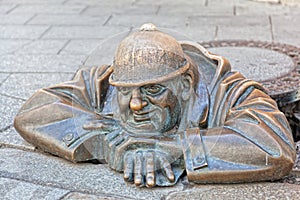 Cumil - statue of man peeking out from under a manhole cover