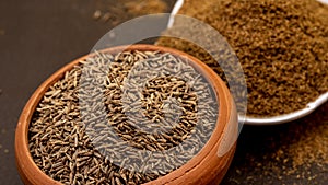 Cumin seeds called Jeera in clay bowl and it`s powder in white bowl on dark background.