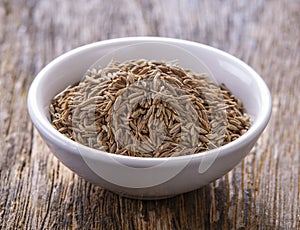 Cumin seeds in white bowl on wooden table