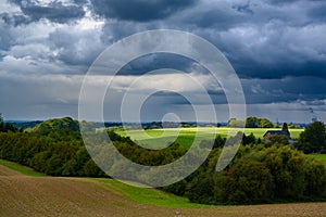 Dark cumulonimbus clouds with sun light spot over green autumn field. photo