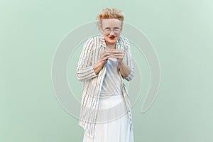 Cunning blonde woman wearing striped shirt and skirt, planning devil prank, looking at camera.