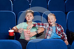 Cunning boy stealing popcorn while friend watching film