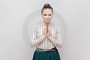 Cunning young adult woman keeps hands together, having slander plan, pondering.