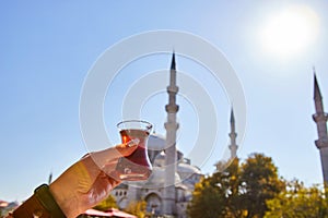 A cup armud of traditional Turkish tea in hand against the background of a mosque in Istanbul