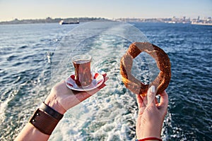 A cup armud of traditional Turkish tea and Simitci a round bagel with sesame seeds in hand against the background of the