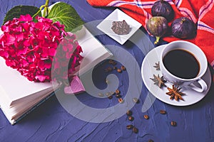 A cup of aromatic coffee, an open book and a branch of hydrangea on a blue background
