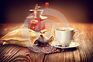 Cup of aromatic coffee on saucer with sack full of roasted coffe