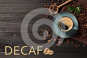 Cup of aromatic decaf coffee and beans on black wooden table, flat lay