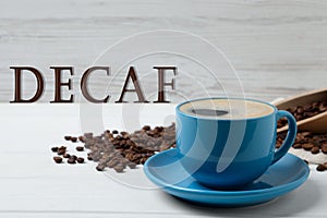 Cup of aromatic decaf coffee and beans on white table