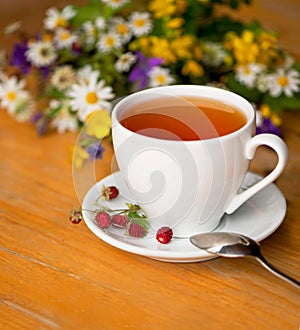 cup of aromatic tea, wild strawberry, bouquet of wild flowers on a wooden background