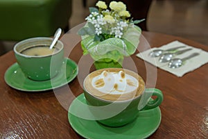 Cup of art cappuccino coffee on desk (Focus on first cup and Background is blur from depth of field)