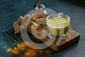 Cup of ayurvedic drink golden milk turmeric latte with curcuma powder, ginger and honey over green texture background