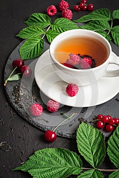 Cup of Berry tea and ripe raspberry, cherry, currant on a black background