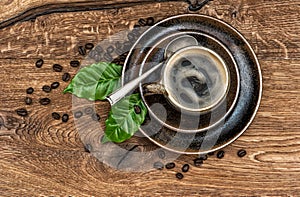 Cup of black coffee with beans and leaves on wooden table