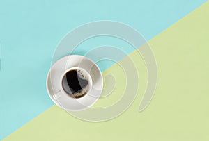 A cup of black coffee on blue and yellow background. View from above.