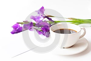 A cup with black coffee and a bouquet of iris flowers are on a light background. photo
