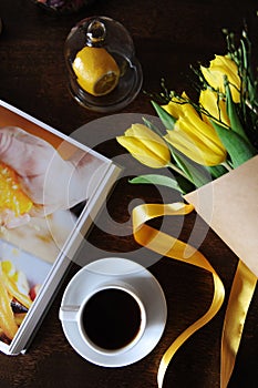 A cup of black coffee and a bouquet of yellow tulips in kraft paper on the table. Book with bright pictures
